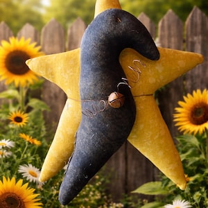May include: A decorative star-shaped hanging ornament. The ornament features a large yellow star with a dark blue, curved accent piece. A small bell and wire detailing add charm. Sunflowers and daisies are in the background.