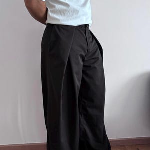 May include: Black wide-leg pants with a high waist and a white short-sleeve t-shirt. The pants have a pleated design and are paired with black sneakers. The outfit is simple and modern.