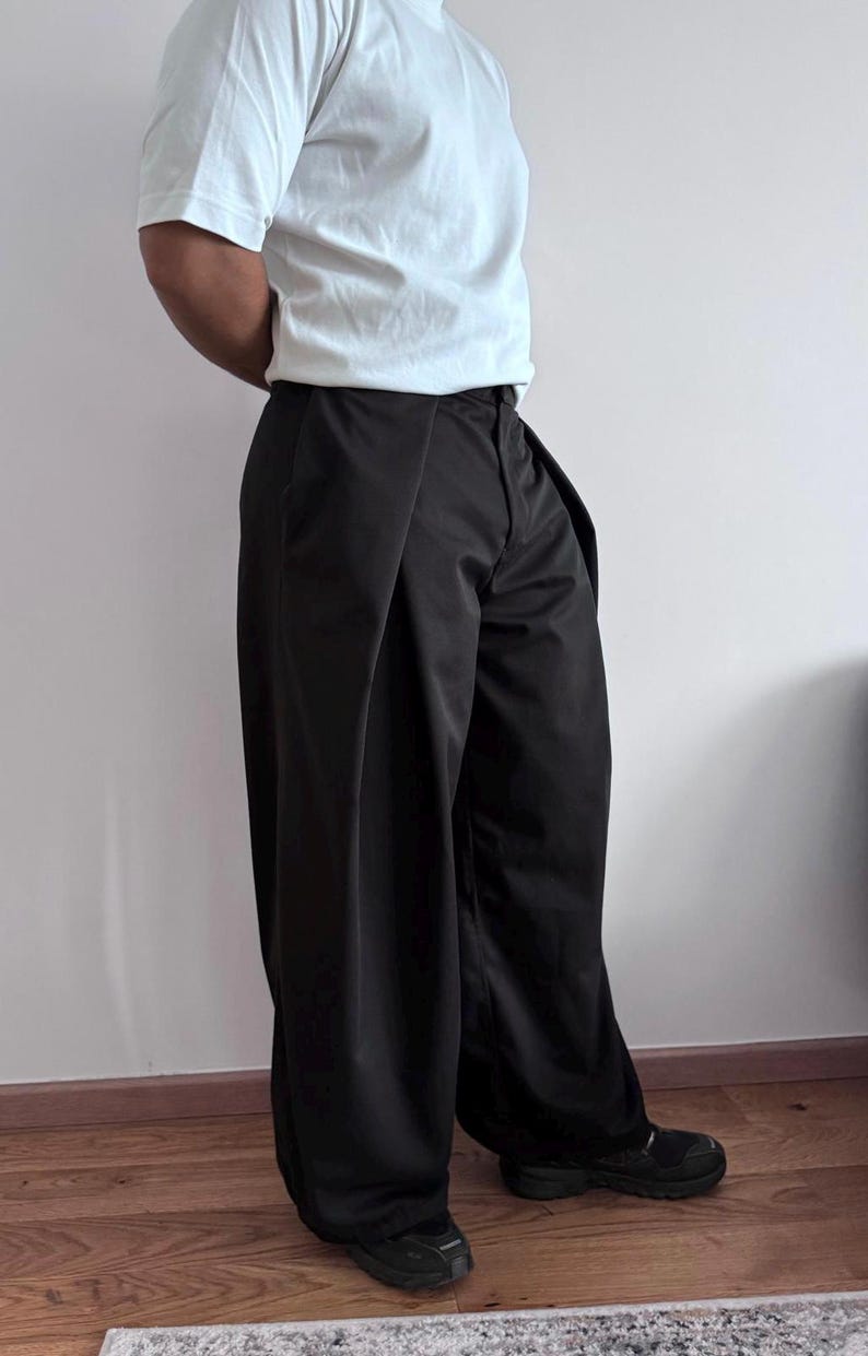 May include: Black wide-leg pants with a high waist and a white short-sleeve t-shirt. The pants have a pleated design and are paired with black sneakers. The outfit is simple and modern.