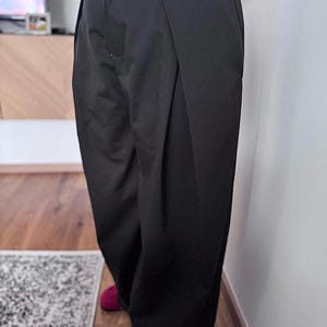 May include: Black wide-leg pants with a high waist. The pants have a pleated front and a relaxed fit. The person is wearing red slippers. The pants are made of a solid, opaque fabric.
