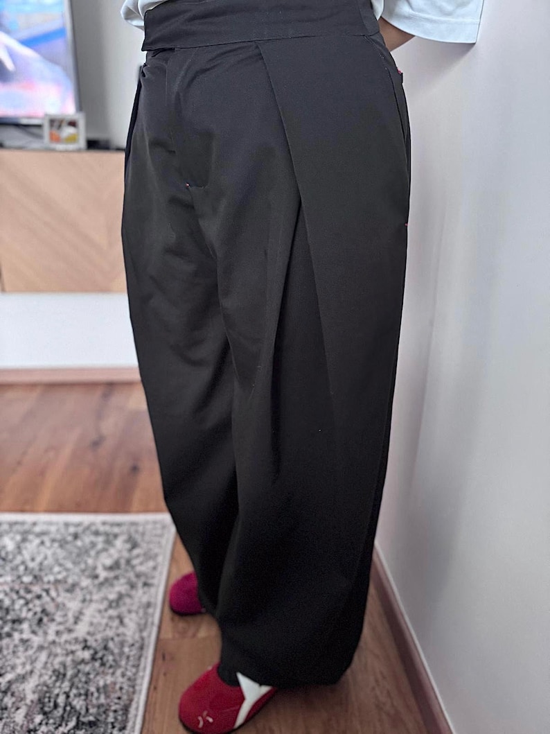 May include: Black wide-leg pants with a high waist. The pants have a pleated front and a relaxed fit. The person is wearing red slippers. The pants are made of a solid, opaque fabric.