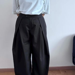 May include: A person wearing a light blue t-shirt and black wide-leg pants. The pants have a pleated design at the waist. The person is also wearing red shoes with white soles.