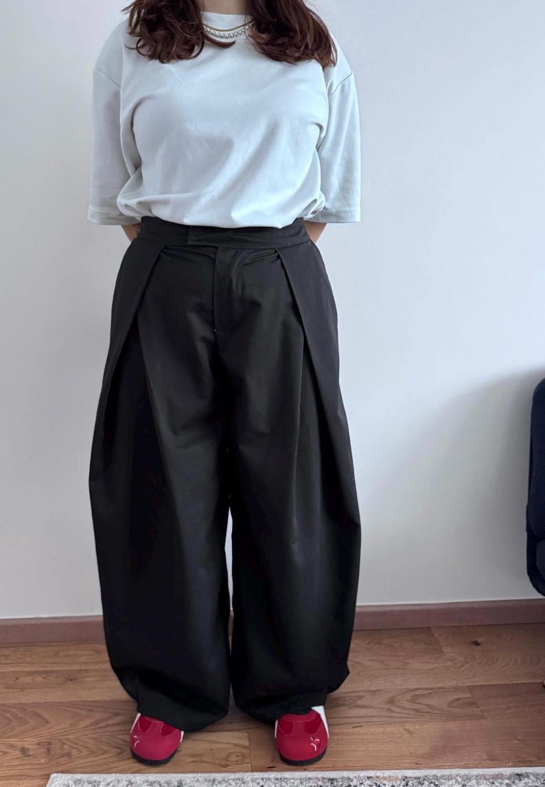May include: A person wearing a light blue t-shirt and black wide-leg pants. The pants have a pleated design at the waist. The person is also wearing red shoes with white soles.
