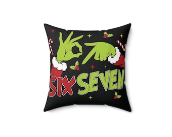 Peut inclure: Coussin carré noir avec des mains vertes formant les chiffres six et sept. Les mots "SIX SEVEN" sont en vert et rouge. Des décorations de houx et de cannes en bonbon complètent le design.