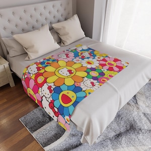 Puede incluir: Una colorida manta con un diseño floral que presenta flores sonrientes y el personaje Hello Kitty. La manta está colocada sobre una cama con almohadas blancas y un cabecero. El diseño incluye varios colores como amarillo, rosa, azul y blanco.