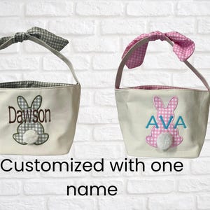 Peut inclure: Deux paniers de P&acirc;ques en toile avec des motifs de lapin. L'un a un n&oelig;ud et une doublure en vichy vert et blanc, avec le nom "Dawson" brod&eacute;. L'autre a un n&oelig;ud et une doublure en vichy rose et blanc, avec le nom "AVA" brod&eacute;.