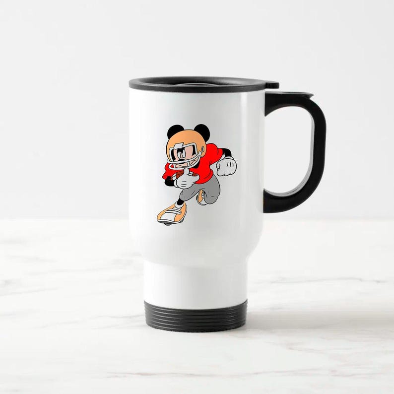 May include: White travel mug with a black handle and rim. The mug features a cartoon illustration of a character in a football uniform, running with the ball. The character is wearing a red jersey, gray pants, and an orange helmet.