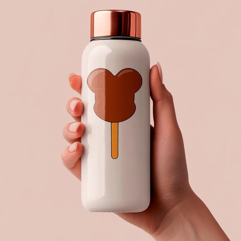 May include: White insulated water bottle with a copper-colored lid. The bottle features a brown cartoon popsicle design on the front. The bottle is held by a person's hand against a light pink background.