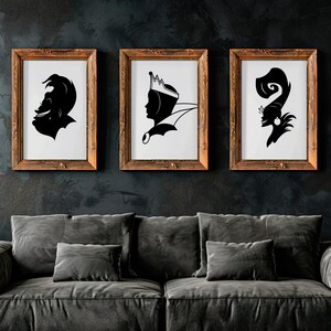 May include: Three framed black and white silhouette art prints. The prints feature stylized profiles of characters, each in a wooden frame. The artwork is displayed above a gray sofa against a dark wall.