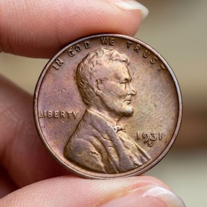Peut inclure: Une pièce de monnaie Lincoln de 1931 S, de couleur cuivrée. La pièce présente le profil d'Abraham Lincoln, le mot "LIBERTY" et l'inscription "IN GOD WE TRUST". L'année "1931" et la marque d'atelier "S" sont visibles.
