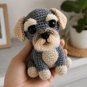 May include: Handmade crocheted Schnauzer dog figurine in grey, beige, and cream. The amigurumi dog has large black eyes, a fluffy beard, and floppy ears. The dog is approximately 13 cm tall.