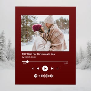 Op de afbeelding: Een rode Spotify-achtige afbeelding met de tekst "All I Want For Christmas Is You" van Mariah Carey. De afbeelding toont een stel in winterkleding, knuffelend in een besneeuwd bos. Inclusief een afspeelknop en een voortgangsbalk.