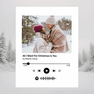 May include: A print in the style of a Spotify track, showing a couple in a snowy scene. The print features the song title "All I Want For Christmas Is You" by Mariah Carey, a play bar, and the Spotify logo. The background shows snow-covered trees.