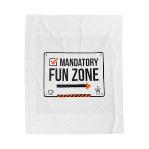 May include: White blanket featuring a black and orange sign that reads "MANDATORY FUN ZONE." The sign includes a checkmark, an arrow, a coffee cup, and a small plant icon. The blanket has a crinkled texture.