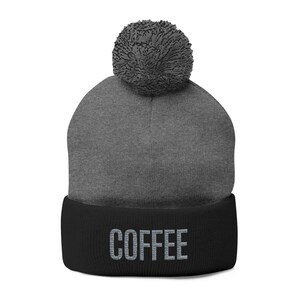 May include: A gray beanie with a black brim and a gray pom-pom. The word "COFFEE" is embroidered in gray on the black brim. This winter hat is a cozy accessory for coffee lovers.