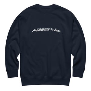 May include: A dark navy blue long-sleeve sweatshirt featuring the word "FREESTYLE" embroidered in a light gray, stylized, elongated font across the center of the chest. The garment has a crew neckline, ribbed cuffs, and a ribbed hemline.
