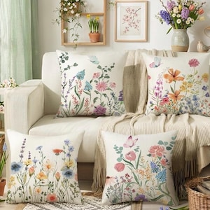 May include: A set of three ceramic mugs with a speckled, cream-colored glaze. Each mug features a different hand-painted design: a blue and green leaf, a yellow flower, and a red berry. The mugs have a simple, rounded shape.