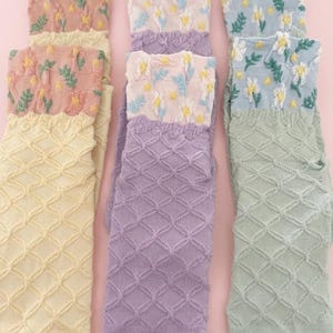 May include: A collection of colorful socks with floral and geometric patterns. The socks feature a variety of colors, including yellow, lavender, pink, and light blue. The tops of the socks have embroidered floral designs, while the lower portions have a diamond pattern.