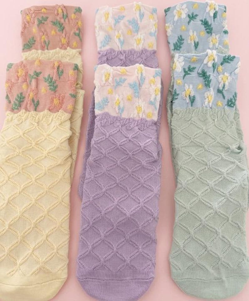 May include: A collection of colorful socks with floral and geometric patterns. The socks feature a variety of colors, including yellow, lavender, pink, and light blue. The tops of the socks have embroidered floral designs, while the lower portions have a diamond pattern.