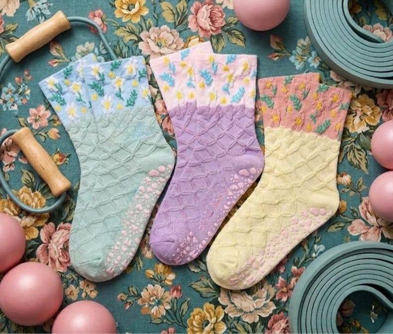 May include: Three pairs of colorful socks with floral patterns and textured soles. The socks are in shades of mint green, lavender, and yellow, with pink and yellow floral designs on the cuffs. A jump rope and exercise balls are also in the image.