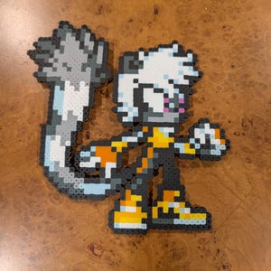 May include: Pixel art figure of a character with white hair, a long gray and white tail, and orange and yellow accents. The figure is made of small, colorful beads and is posed in a dynamic stance.
