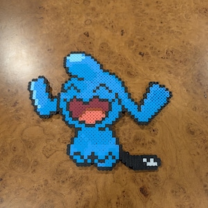 May include: A blue pixel art character with a wide smile and outstretched arms. The character is made of small, round beads in shades of blue, with a red mouth and black accents. The character has a tail with a white square at the end.