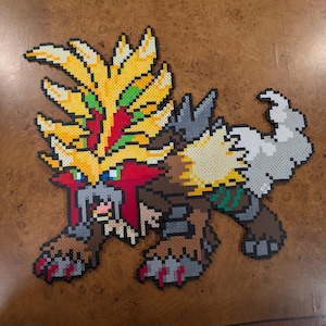 Könnte beinhalten: Ein farbenfrohes Pixelkunstwerk, das ein mythisches Wesen darstellt, mit einer lebendigen Palette aus Gelb, Rot, Braun, Grau und Grün. Das Kunstwerk wurde wahrscheinlich mit Bügelperlen hergestellt und zeigt ein detailliertes Design der Form des Wesens.