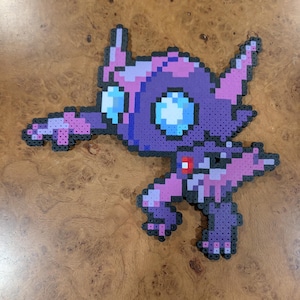 May include: A pixel art figure crafted from purple, pink, and light blue plastic beads. The creature features a large head with two pointed ears, wide circular eyes, and a dynamic pose with one arm extended outward and a small red accent on its chest.
