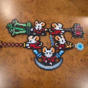 Pode incluir: Cinco figuras de pixel art feitas de contas de plástico, cada uma representando um rato branco vestindo uma roupa vermelha. Os ratos estão dispostos em um grupo, com cada figura segurando uma arma ou ferramenta diferente, incluindo um cajado.