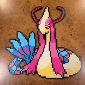 May include: A pixel art creation made of fused plastic beads depicting a serpentine creature with a cream-colored body, long flowing pink hair-like structures, and large blue fan-shaped fins. The design features a pointed head and red eyes.