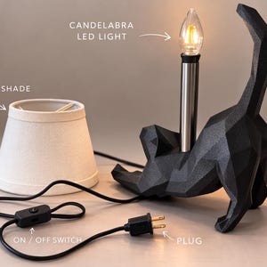 K&ouml;nnte beinhalten: Schwarze Katzen-Tischlampe mit Leinen-Lampenschirm. Die Lampe verf&uuml;gt &uuml;ber eine LED-Kerzenlicht-Gl&uuml;hbirne und einen Ein-/Ausschalter. Der Stecker ist ein Standardstecker.