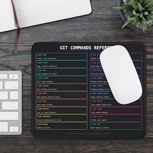 May include: A rectangular black mouse pad featuring a Git commands reference guide with colorful text and command descriptions organized in two columns. The pad displays various terminal commands like git init, git clone, and git status.