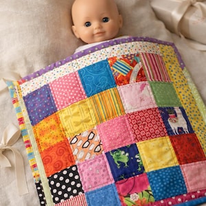 May include: A colorful patchwork baby quilt with a variety of patterned squares in shades of pink, blue, yellow, and orange. The quilt is trimmed with a purple border and has white ribbon ties. A doll is partially visible.