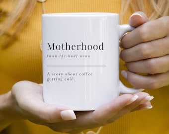 May include: White ceramic mug with the word "Motherhood" in a black font. Below the word is the phonetic pronunciation and the word "noun". The mug also has the text "A story about coffee getting cold."