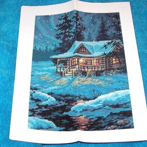 May include: A cross-stitch pattern depicting a cosy cabin nestled in a snowy forest at night. The cabin has warm lights in the windows and a snowy roof. The forest is dark blue with white snow on the ground. The sky is dark blue with white stars.