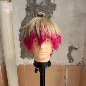 May include: A short, layered synthetic wig featuring a two-tone colour scheme with light blonde hair on the top and vibrant hot pink hair on the bottom layers. The wig is styled with a textured, choppy cut and a small, upright hair tuft.