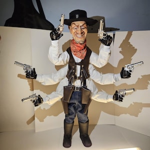 Puede incluir: Una marioneta con temática de vaquero con seis brazos, cada uno sosteniendo pistolas de juguete plateadas. La marioneta lleva un sombrero negro, un pañuelo rojo, un chaleco marrón y vaqueros azules. La cara muestra una amplia sonrisa exagerada.