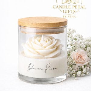 May include: A white rose-shaped candle in a clear glass jar with a wooden lid. The candle is labeled "Bloom Rose" in script. The background includes a small bouquet of white flowers and a logo that says "Candle Petal Gifts by Neha."