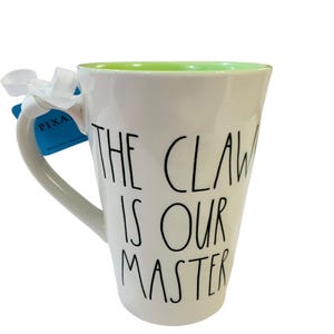Pu&ograve; includere: Una tazza in ceramica bianca con interno verde chiaro. L'esterno presenta un testo nero scritto a mano che recita THE CLAW IS OUR MASTER. Un nastro bianco &egrave; legato al manico e un'etichetta blu con la parola PIXAR &egrave; attaccata al manico.