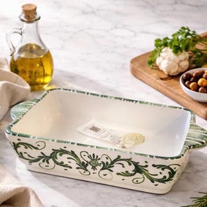 Könnte beinhalten: Eine rechteckige, cremefarbene Keramik-Backform mit grünen Blumen- und Rankenmustern. Die Form hat einen grünen Rand und Griffe. Eine Glasflasche Öl und ein Schneidebrett mit Gemüse befinden sich im Hintergrund.