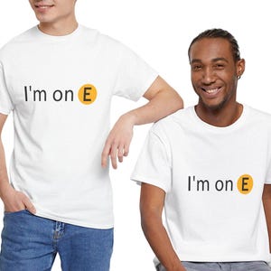 May include: Two people wearing white t-shirts with the text "I'm on E" in black and a yellow circle with a black "E". The t-shirts are paired with blue jeans. The background is white.