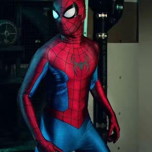 Pode incluir: Um traje vermelho e azul do Homem-Aranha. O traje apresenta um torso e cabe&ccedil;a vermelhos com um emblema de aranha preta no peito. Os bra&ccedil;os e pernas s&atilde;o azuis com detalhes de teia de aranha vermelha. A m&aacute;scara tem lentes brancas.