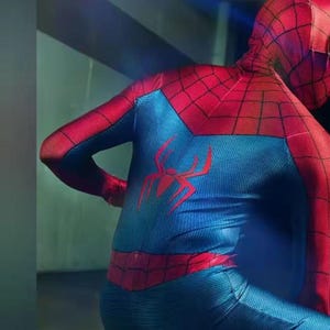 Pode incluir: Um traje vermelho e azul do Homem-Aranha. O traje apresenta um emblema de aranha vermelha nas costas e um padr&atilde;o de teia de aranha nas se&ccedil;&otilde;es vermelhas. O torso &eacute; azul. A pessoa est&aacute; usando um traje completo.