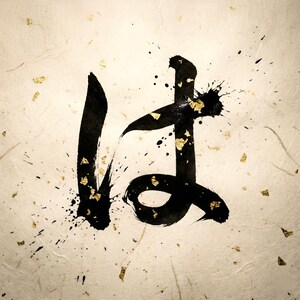 以下が含まれることがあります： 日本の書道作品のクローズアップ。黒インクで描かれた文字「は」が、質感のあるオフホワイトの背景に映えます。黒インクの飛沫と金箔が文字を囲み、印象的なコントラストを生み出しています。