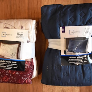 May include: Two packaged king-size pillow shams. One is cream-colored with a floral pattern and the other is navy blue with a quilted design. Each package includes a king sham, with dimensions of 24 in x 40 in (61 cm x 101.6 cm) and 20 in x 36 in (50.8 cm x 91.4 cm) respectively.