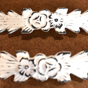 May include: Two white, distressed-finish decorative drawer pulls. Each pull features a floral design with a central flower and leaf accents. The pulls are approximately 6 inches long.