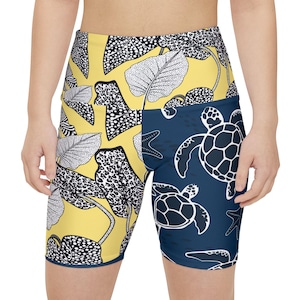 May include: High-waisted athletic shorts featuring a split-panel design. The left side is yellow with a black and white stippled leaf pattern, while the right side is dark blue with a white graphic print of sea turtles and starfish.