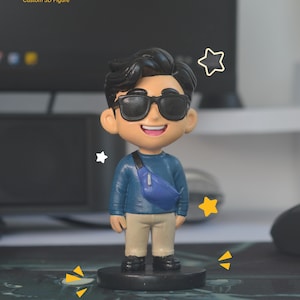 May include: A custom 3D figure of a person wearing sunglasses, a blue shirt, and tan pants, with a blue fanny pack. The figure is standing on a black base, with the text "Say Hi! Custom 3D Figure" in the top left corner.