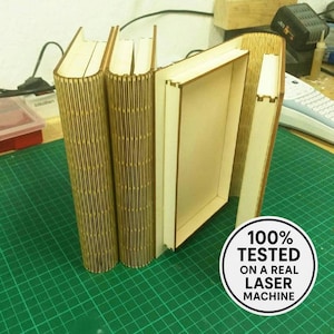 May include: Wooden book-shaped box with a laser-cut design. The box is open, revealing a hollow interior. The image includes the text "100% TESTED ON A REAL LASER MACHINE" in a circular badge. The box is made of light brown wood.