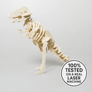 Puede incluir: Un rompecabezas de esqueleto de Tyrannosaurus Rex de madera de color claro. El modelo de dinosaurio está hecho de piezas entrelazadas y se encuentra sobre una superficie blanca. El texto de la imagen dice "100% TESTED ON A REAL LASER MACHINE."